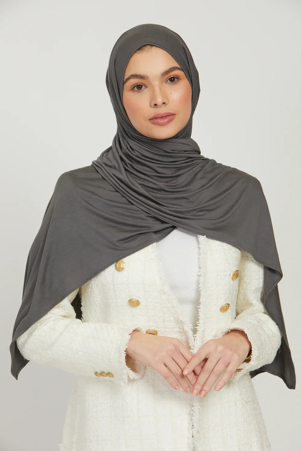 Eine Frau trägt einen einfarbigen grauen Jersey-Hijab und eine weiße strukturierte Jacke.