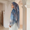 Eine Frau trägt einen eleganten bedruckten Baumwoll-Rayon-Hijabschal in Blau- und Grautönen in einem hellen Flur.