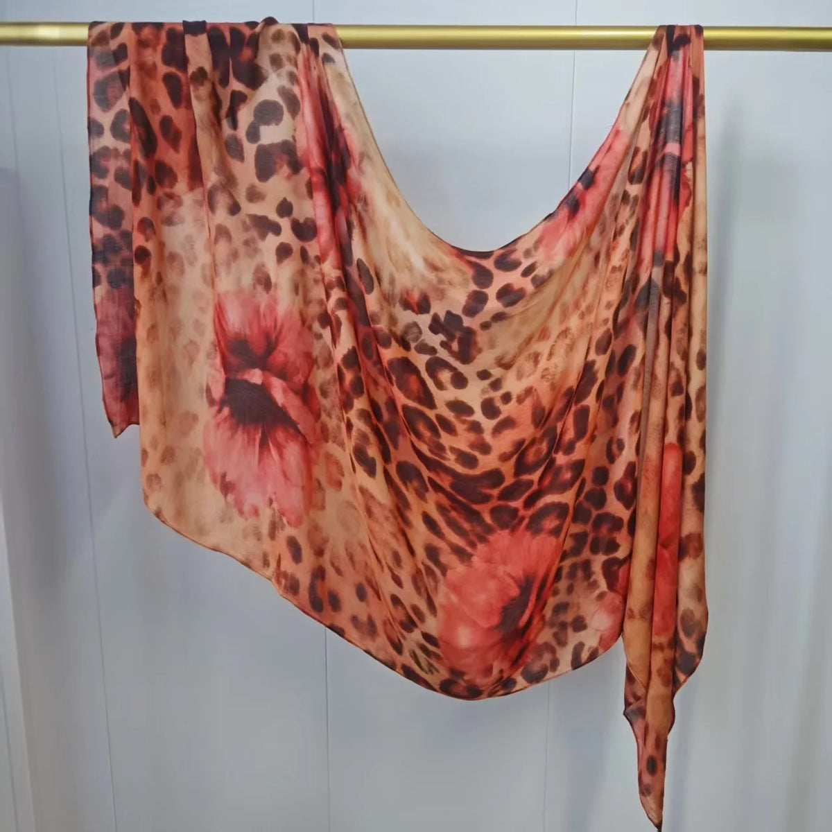 Fließender, mehrfarbiger Hijab-Schal mit Leoparden- und Blumenmuster hängt an einem Gestell.