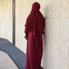 Eine Frau in einem maroonfarbenen Abaya und Khimar-Set vor einer hellen Wand.