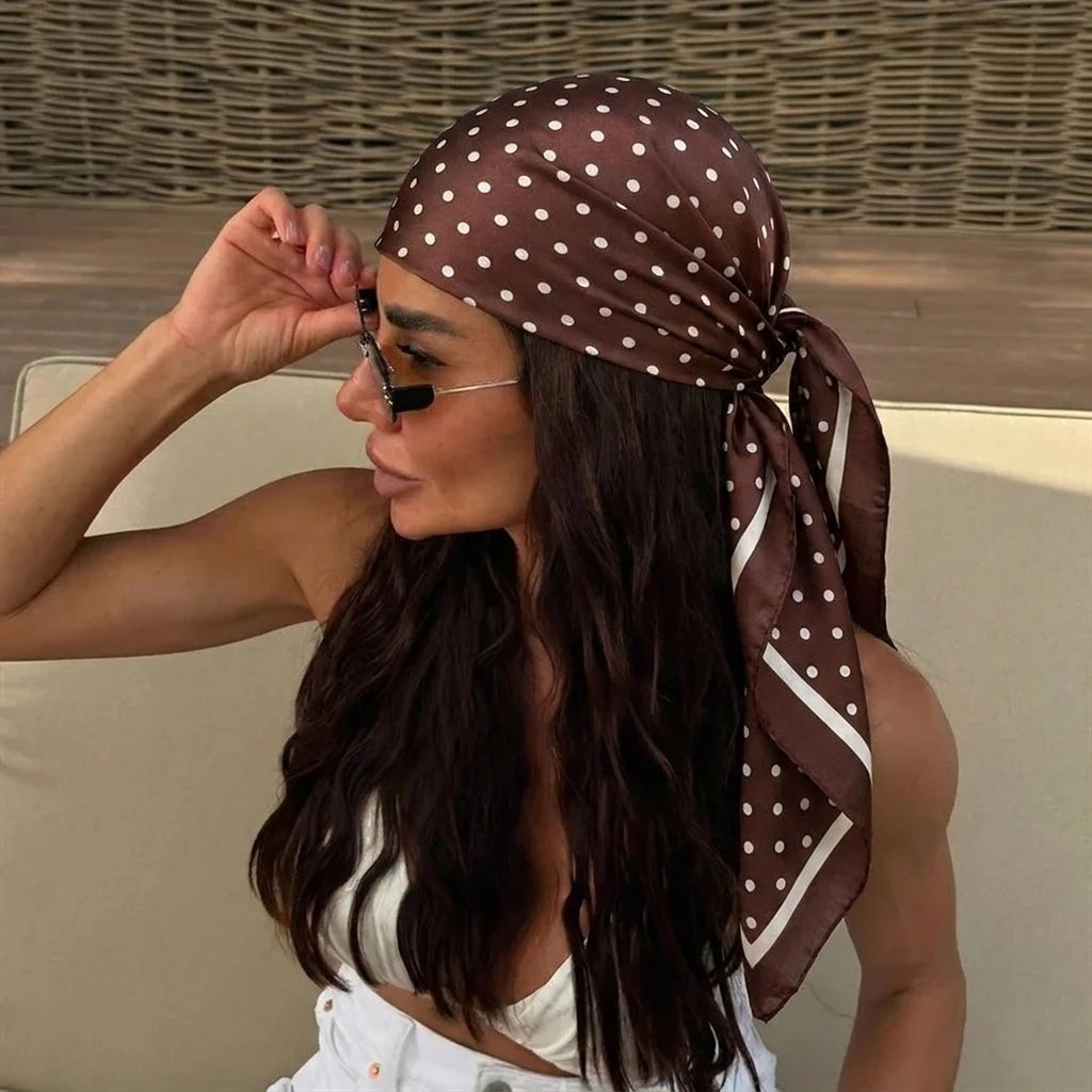 A woman wearing a brown polka dot silk scarf tied around her hair and neck.