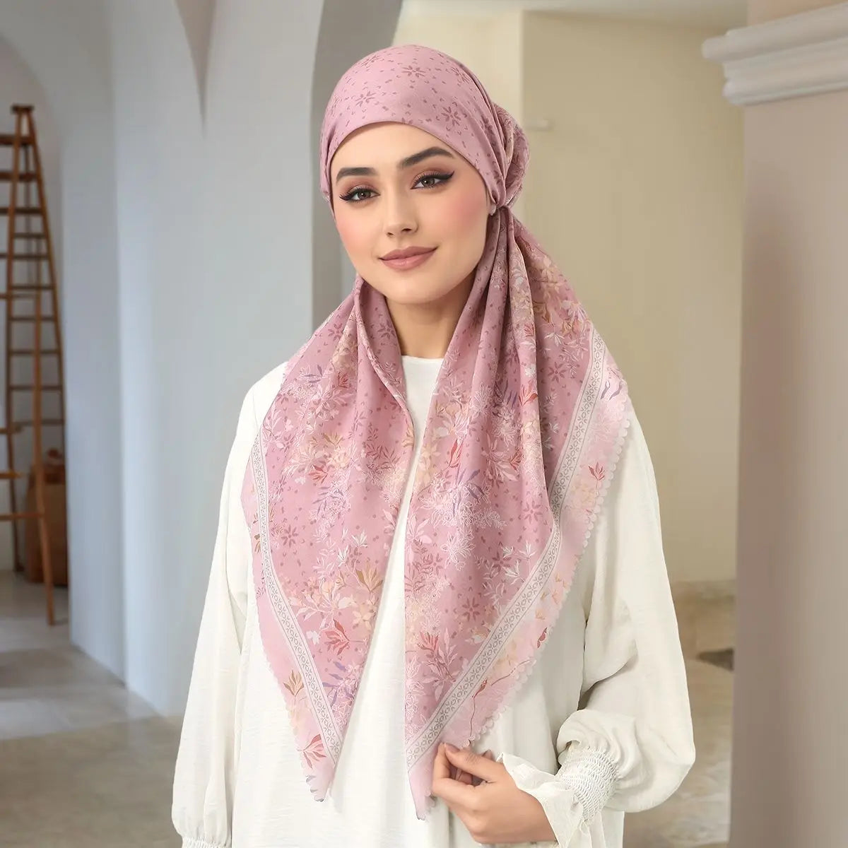 Eine Frau trägt einen rosa gemusterten Voile-Hijab und ein weißes Oberteil.