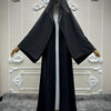 Schwarzes Abaya-Cardigan-Kleid mit Polka Dots auf weißem Mannequin vor dekorativer Wand.