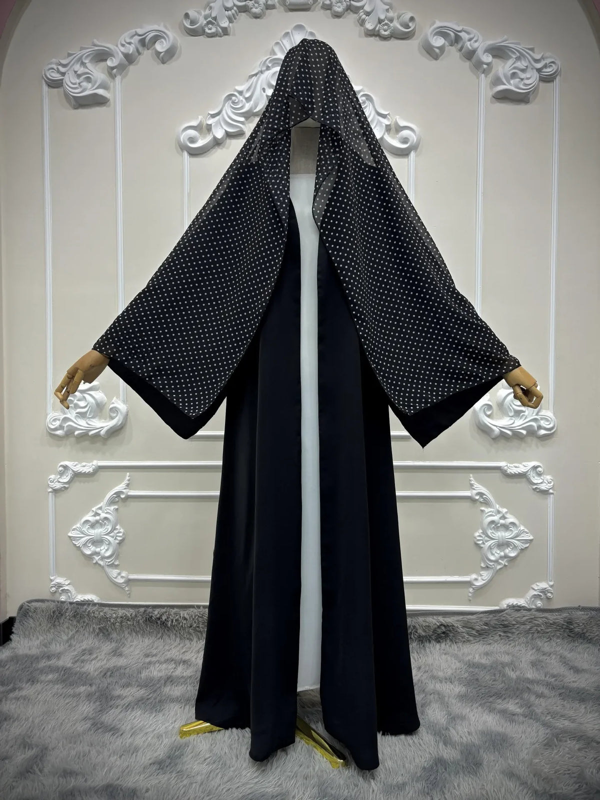 Schwarzes Abaya-Cardigan-Kleid mit Polka Dots auf weißem Mannequin vor dekorativer Wand.