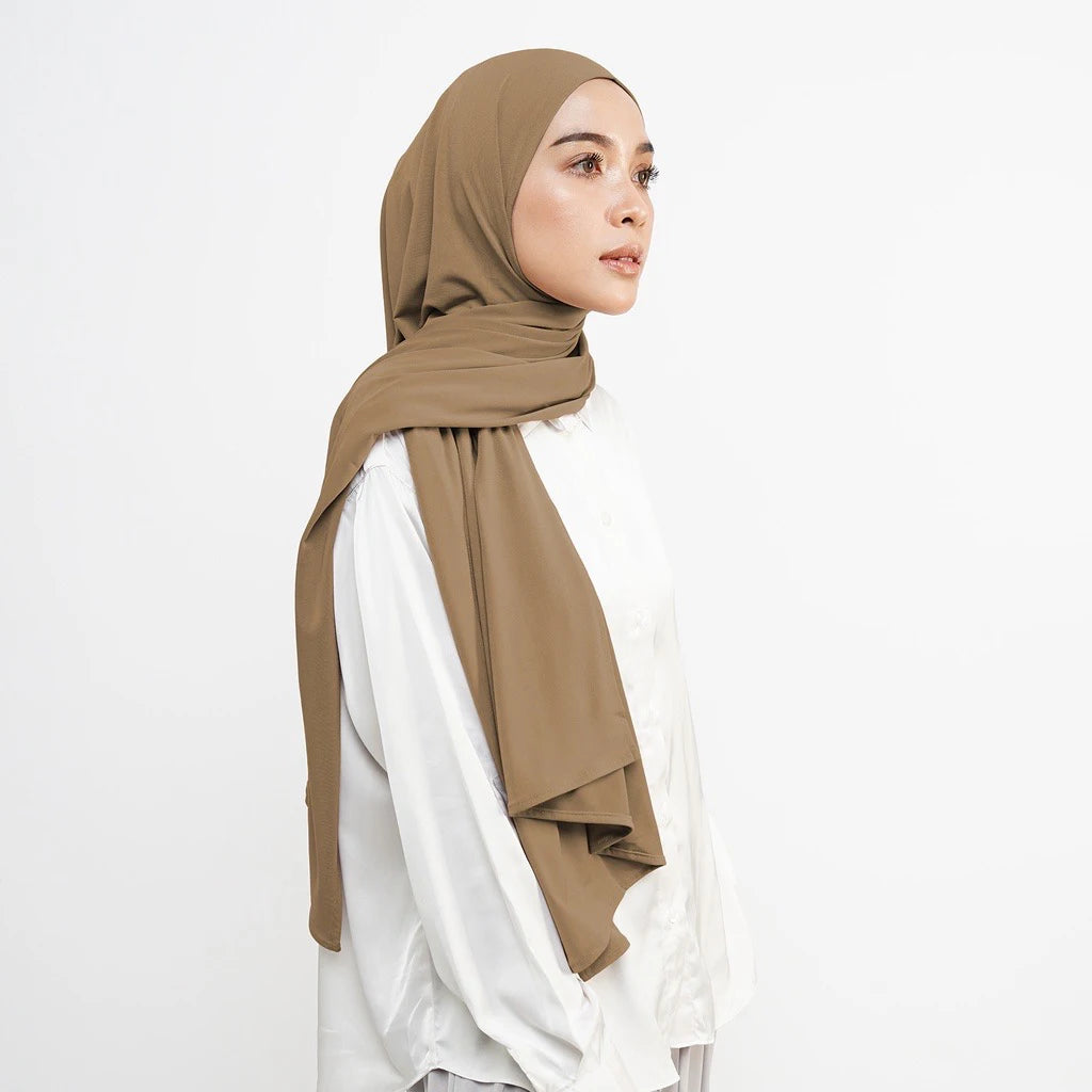 Eine Frau trägt einen beigen weichen Baumwoll-Jersey Instant-Hijab-Schal und ein weißes Oberteil.