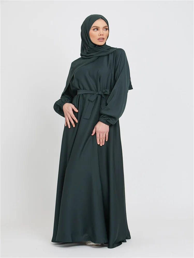Eine Frau trägt eine dunkelgrüne marokkanische Kaftan-Abaya mit Kapuze und Gürtel.