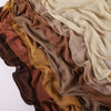 Pile de foulards ou châles en crêpe de rayon drapés et fluides dans des tons terreux : brun, or, beige et olive.