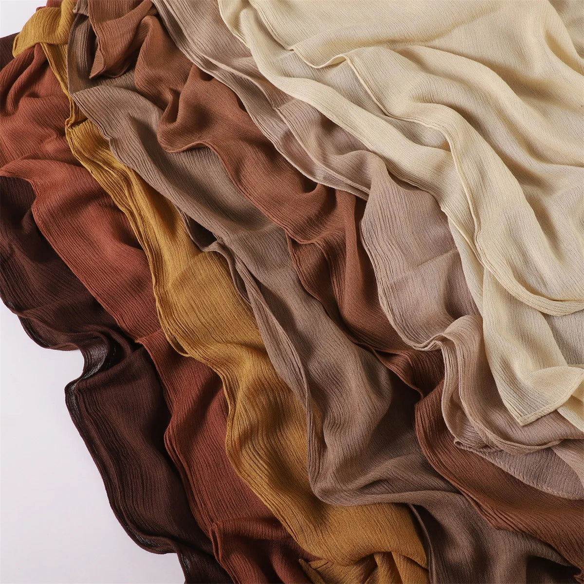 Pile de foulards ou châles en crêpe de rayon drapés et fluides dans des tons terreux : brun, or, beige et olive.
