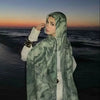 Eine Frau trägt einen eleganten bedruckten Baumwoll-Rayon-Hijabschal mit grünem Muster und blickt zum Meer bei Sonnenuntergan