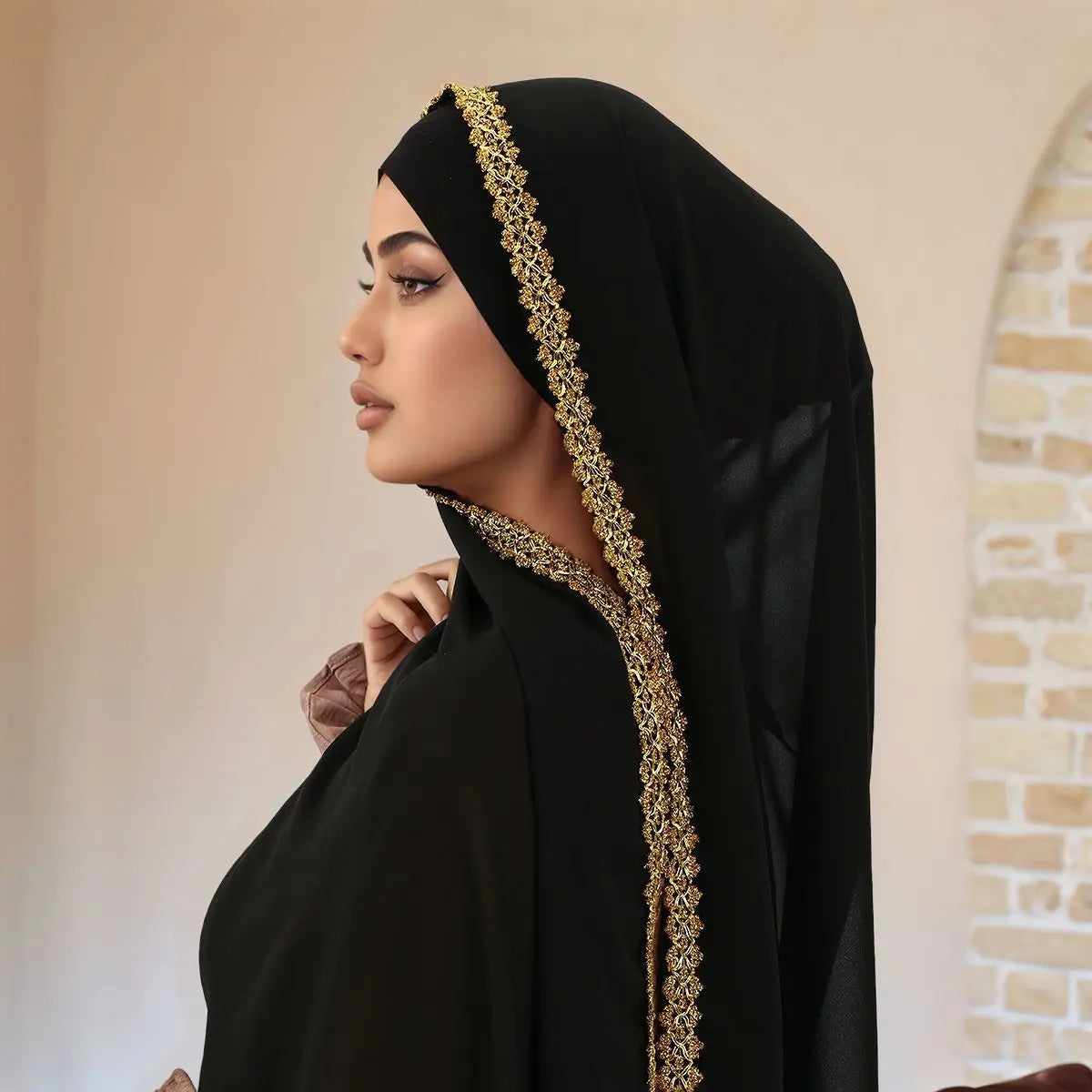 Una mujer vistiendo un elegante hiyab de gasa negra adornado con detalles de strass dorados.