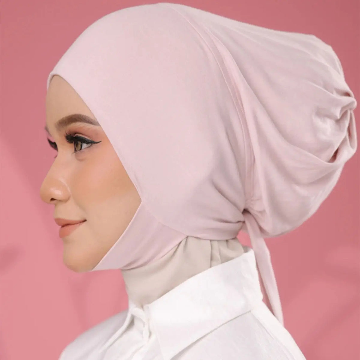 A woman wearing a light pink elegant cotton polyester inner hijab cap scarf and white clothing.