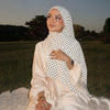 Eine Frau trägt ein cremefarbiges, langärmeliges Jersey-Hijab mit schwarzen Polka Dots, sitzt draußen bei Sonnenuntergang.