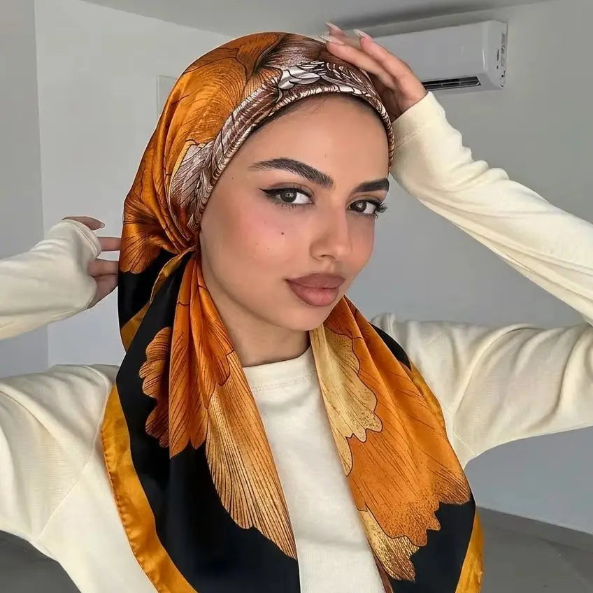 Eine Frau modelliert einen orange-schwarz gedruckten Satin-Seid-Hijabschal um ihren Hals.