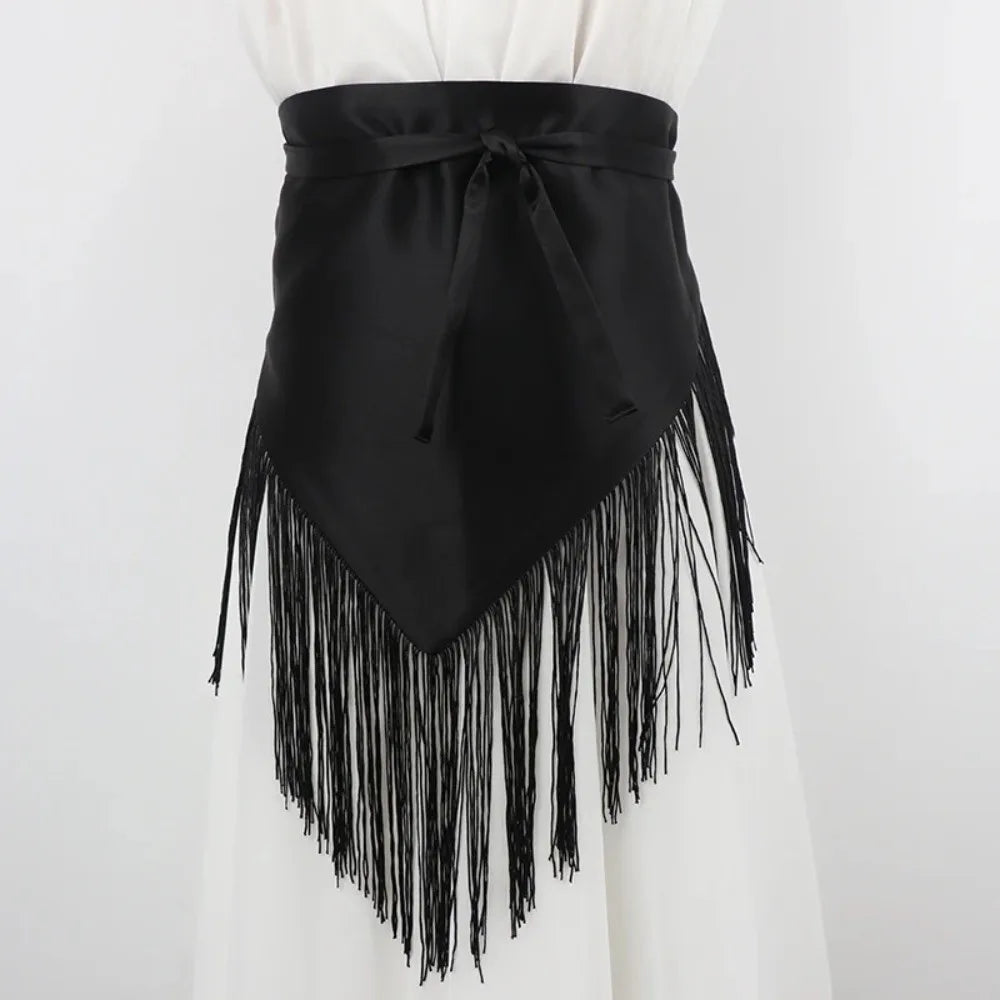 Ceinture triangle en satin noir avec longues pompons noirs attachée autour d'un vêtement blanc.