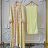 Une longue abaya jaune pâle avec des détails en dentelle florale rose, présentée sur une perche dorée dans un cadre décoratif