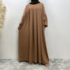 Eine Frau in einem eleganten, langen, erdigen islamischen Kleid mit weiten Ärmeln und fließender Silhouette.