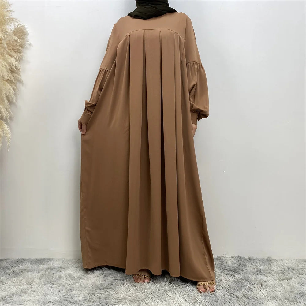 Eine Frau in einem eleganten, langen, erdigen islamischen Kleid mit weiten Ärmeln und fließender Silhouette.