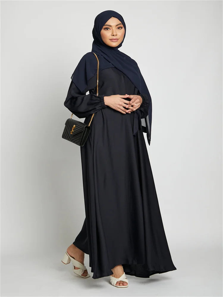 Eine Frau in einem schwarzen marokkanischen Kaftan-Abaya und Hijab vor hellem Hintergrund.