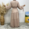 Abrigo cardigan de abaya con cuentas beige, mostrado contra una pared blanca con hierbas secas.