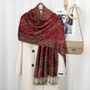 Chal vintage de bordado paisley rojo intenso sobre un blazer crema, exhibido con anillos de madera.