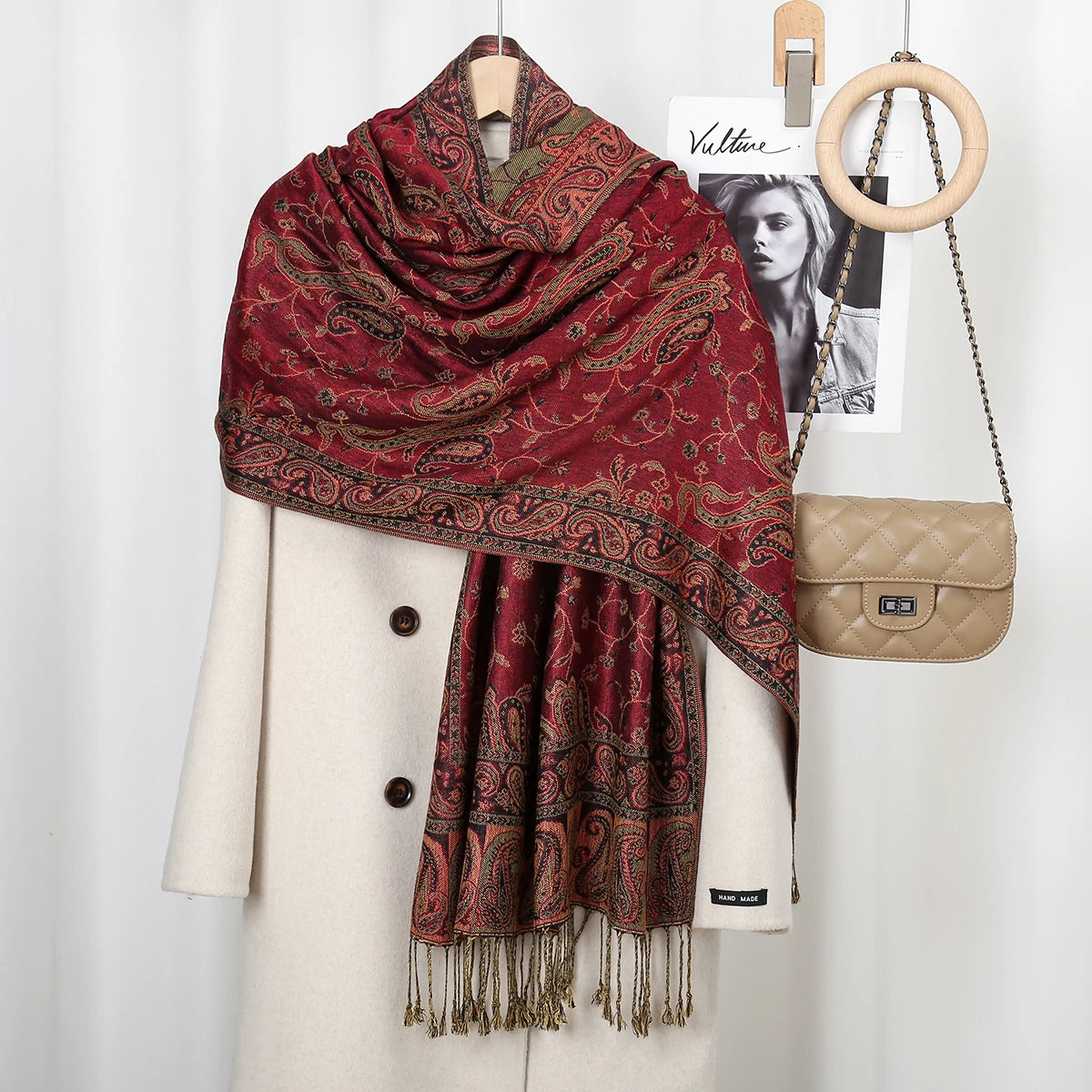 Chal vintage de bordado paisley rojo intenso sobre un blazer crema, exhibido con anillos de madera.