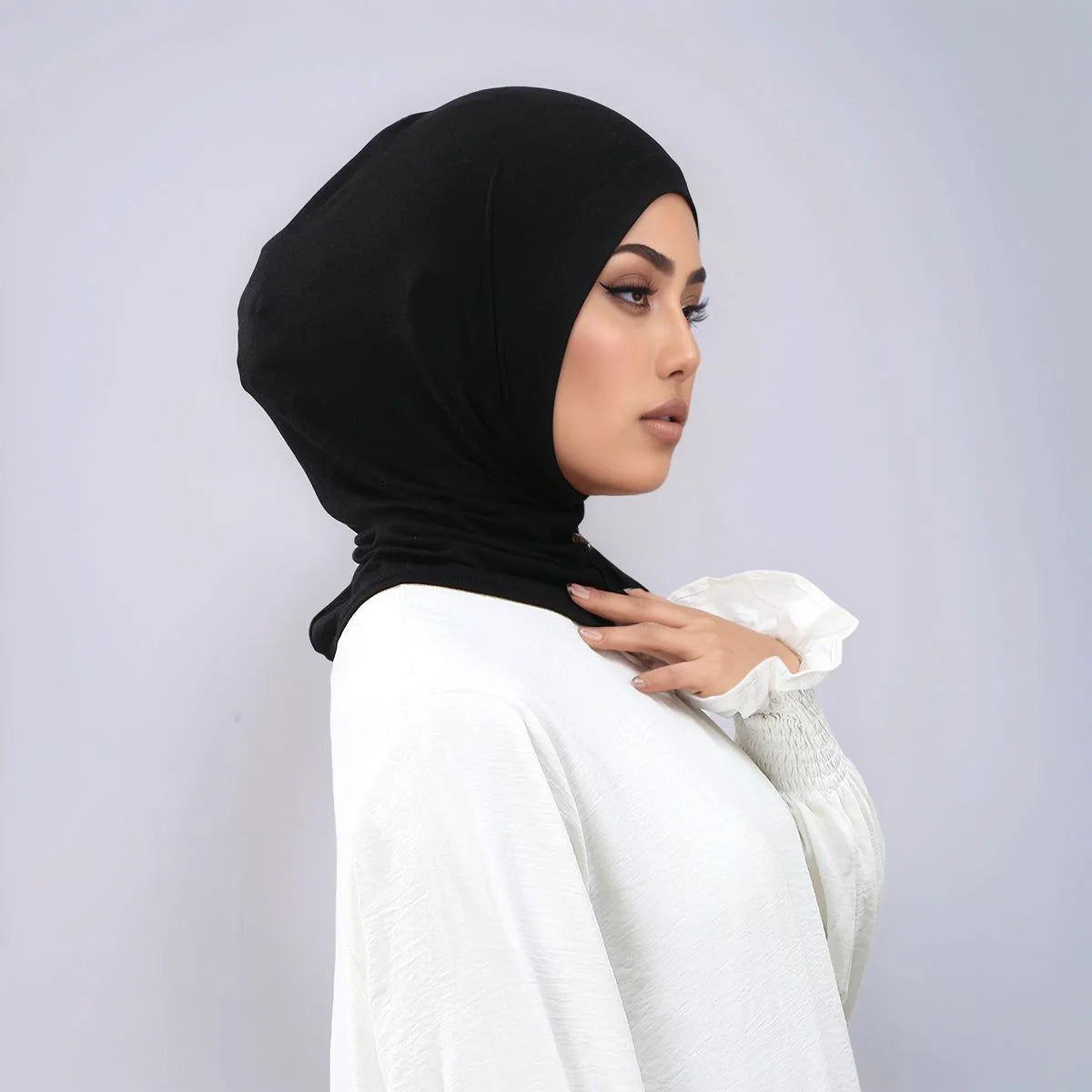 Eine Frau trägt einen schwarzen Instant-Turban-Hijab unter einem weißen langärmeligen Top.