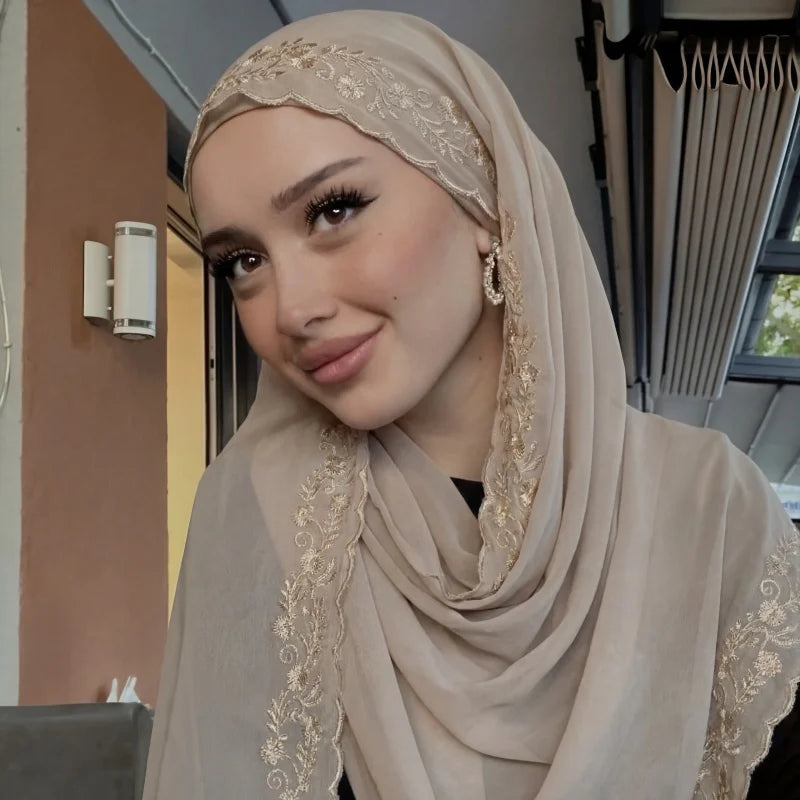 Une femme portant un foulard chiffon beige à bordure de dentelle à cils, regardant l'appareil photo.