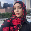 Una mujer vistiendo un hiyab negro con estampado floral rojo, mirando directamente a la cámara.