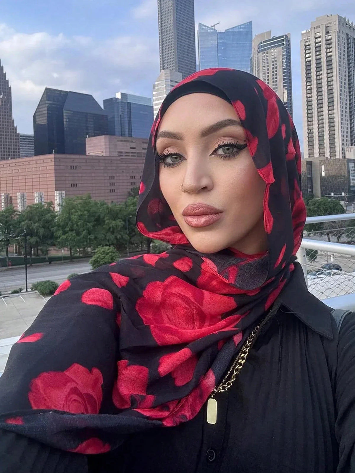 Una mujer vistiendo un hiyab negro con estampado floral rojo, mirando directamente a la cámara.