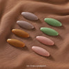 A set of eight solid color brooch pins in grey and green shades arranged on a brown fabric.