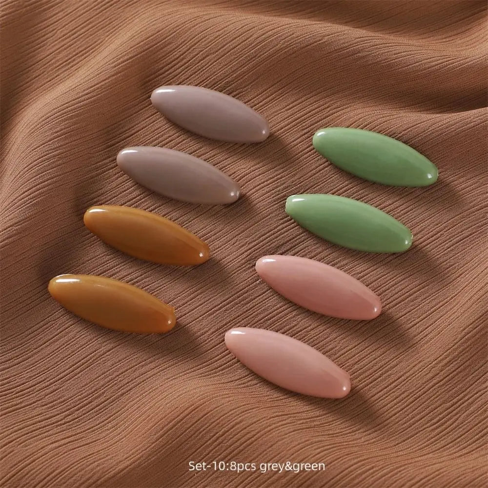 A set of eight solid color brooch pins in grey and green shades arranged on a brown fabric.