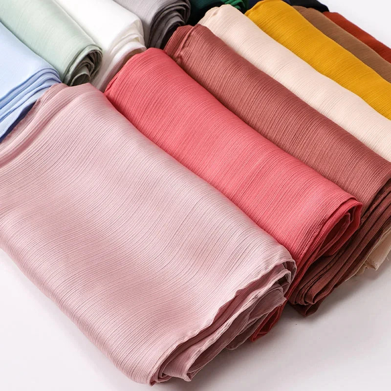 Ein Stapel von rosa, beige und gelben Satin-Crinkle-Hijab-Schals für Frauen.