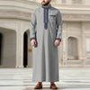 Un hombre vistiendo una jubba thobe casual de color gris claro bordada con cuello alto y puños a juego.