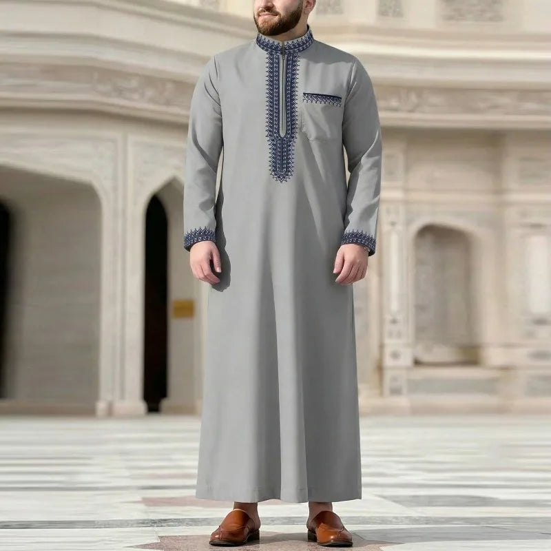 Un hombre vistiendo una jubba thobe casual de color gris claro bordada con cuello alto y puños a juego.