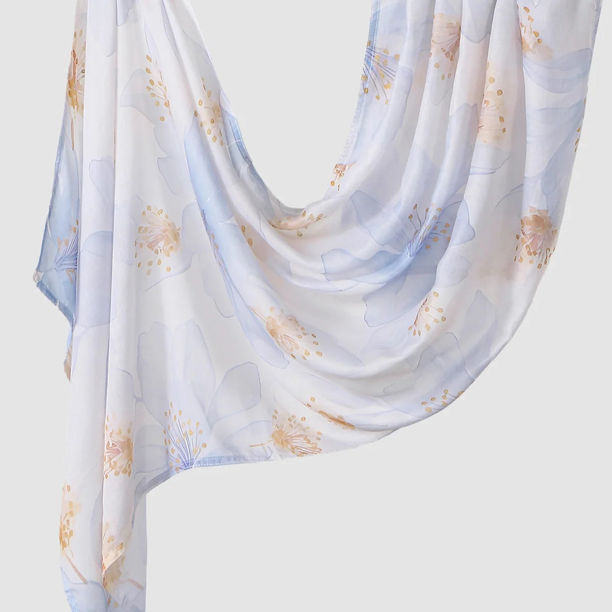 A flowing white linen hijab scarf with a soft blue floral print and gold accents.