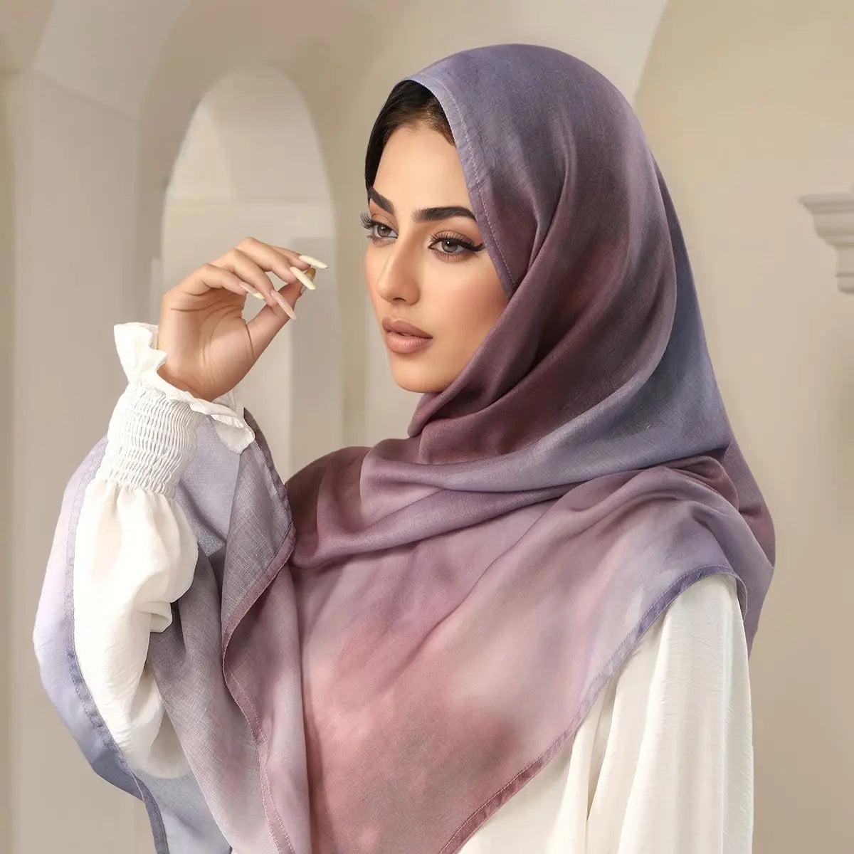 Eine Frau trägt einen lila bedruckten Baumwoll-Rayon-Hijabschal mit weißen Manschetten und einem weißen Oberteil.