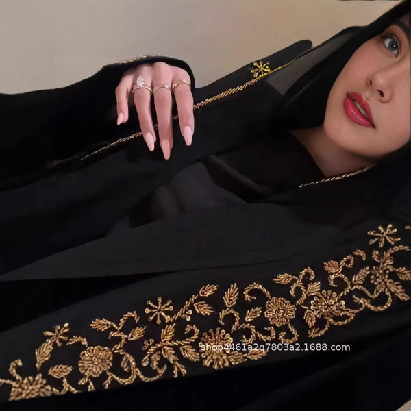 A woman wearing a black abaya with gold floral embroidery and gold rings.