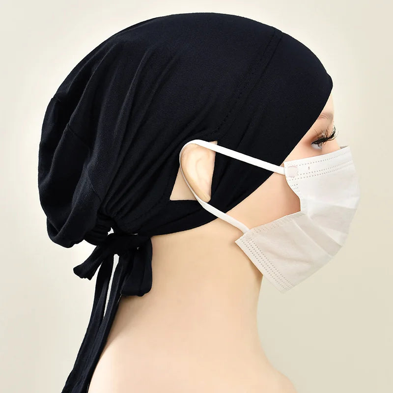Eine Frau trägt eine schwarze Jersey-Baumwoll-Hijabkappe und eine weiße Schutzmaske.