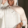 Una mujer vistiendo un pañuelo de hijab de jersey modal beige premium y una blusa blanca de manga larga.