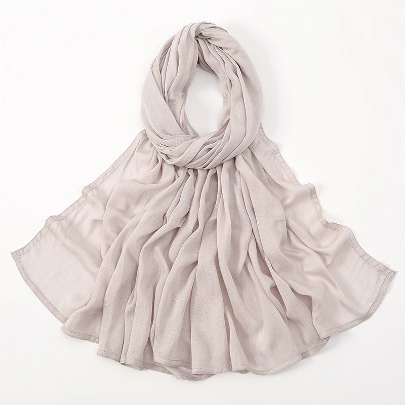 Pañuelo de algodón rayón beige claro, drapeado alrededor del cuello y cayendo sobre los hombros.