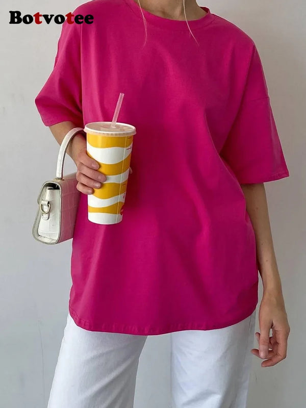 A person wearing a bright pink oversized cotton basic t-shirt holds a striped yellow cup.