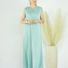 A woman wearing a flowing mint green modest abaya dress standing in front of decorative dried floral arrangements.