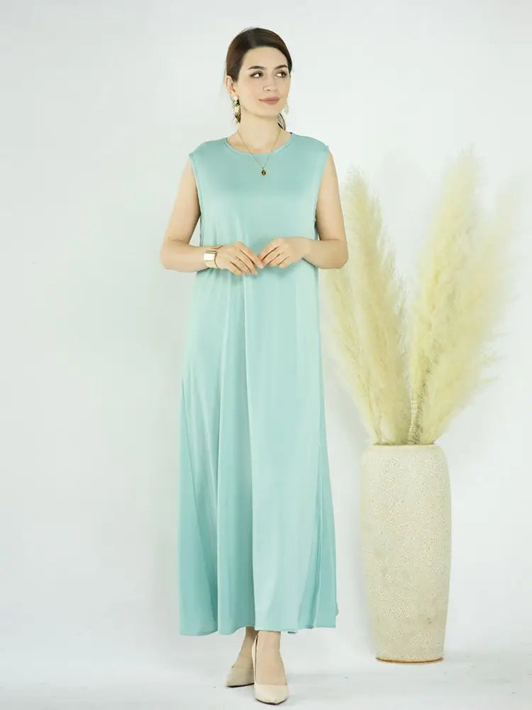 A woman wearing a flowing mint green modest abaya dress standing in front of decorative dried floral arrangements.