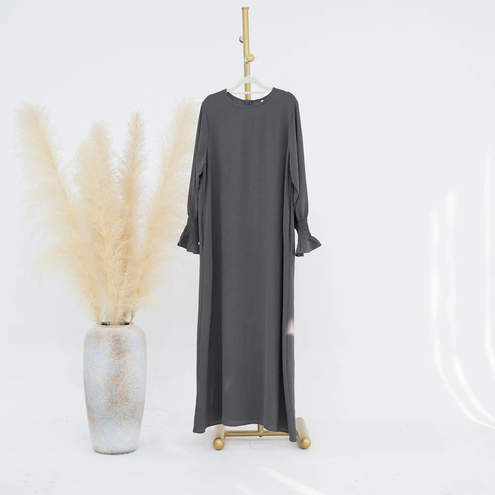 Vestido abaya gris carbón holgado colgado en una percha junto a un manojo de pampas secas beige.