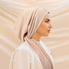 A woman wearing a beige solid color turban hijab cap and white clothing, shown in profile.