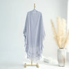 A light purple ruffled two-layer chiffon hijab hanging on a wooden hanger against a white wall.