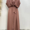 Eine Frau trägt ein fließendes, offenes Abaya-Kaftan in staubrosa Farbe mit einem weißen Hijab.