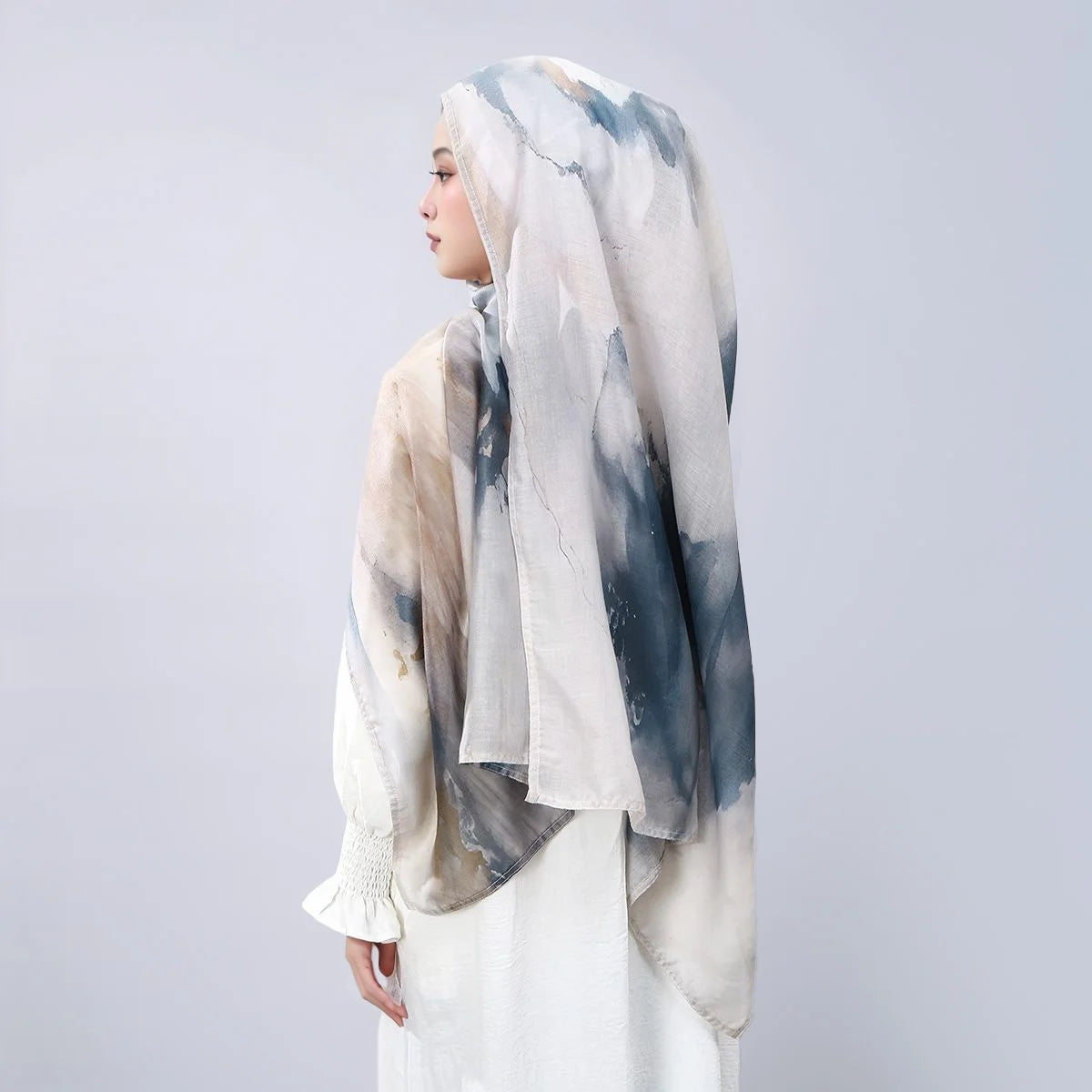 Eine Frau trägt einen Leinen-Baumwoll-Hijab-Schal mit Aquarelldruck in Blau- und Beige-Tönen.