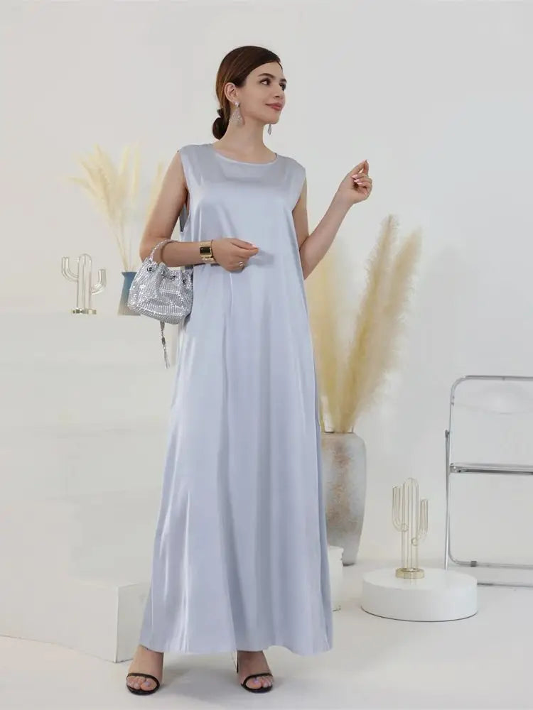A woman wearing a flowing, light blue modest abaya dress stands against a white background.