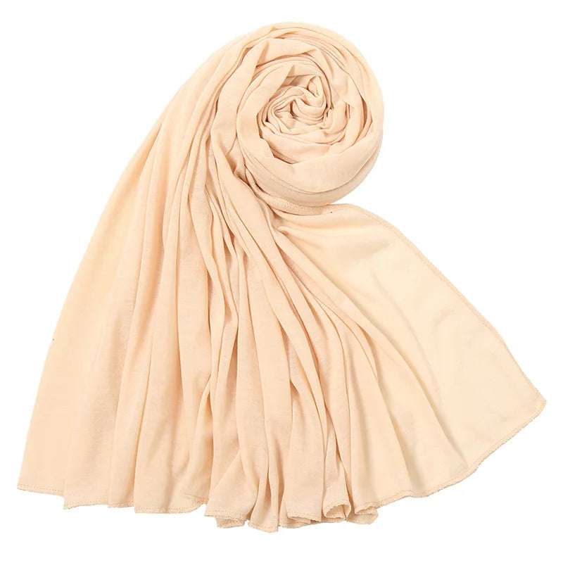 Un foulard hijab en jersey de coton beige clair, roulé et drapé, montrant des plis doux.